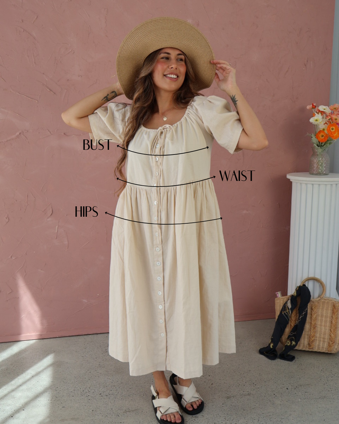 Woman wearing a beige dress with labeled measurements against a pink wall.
