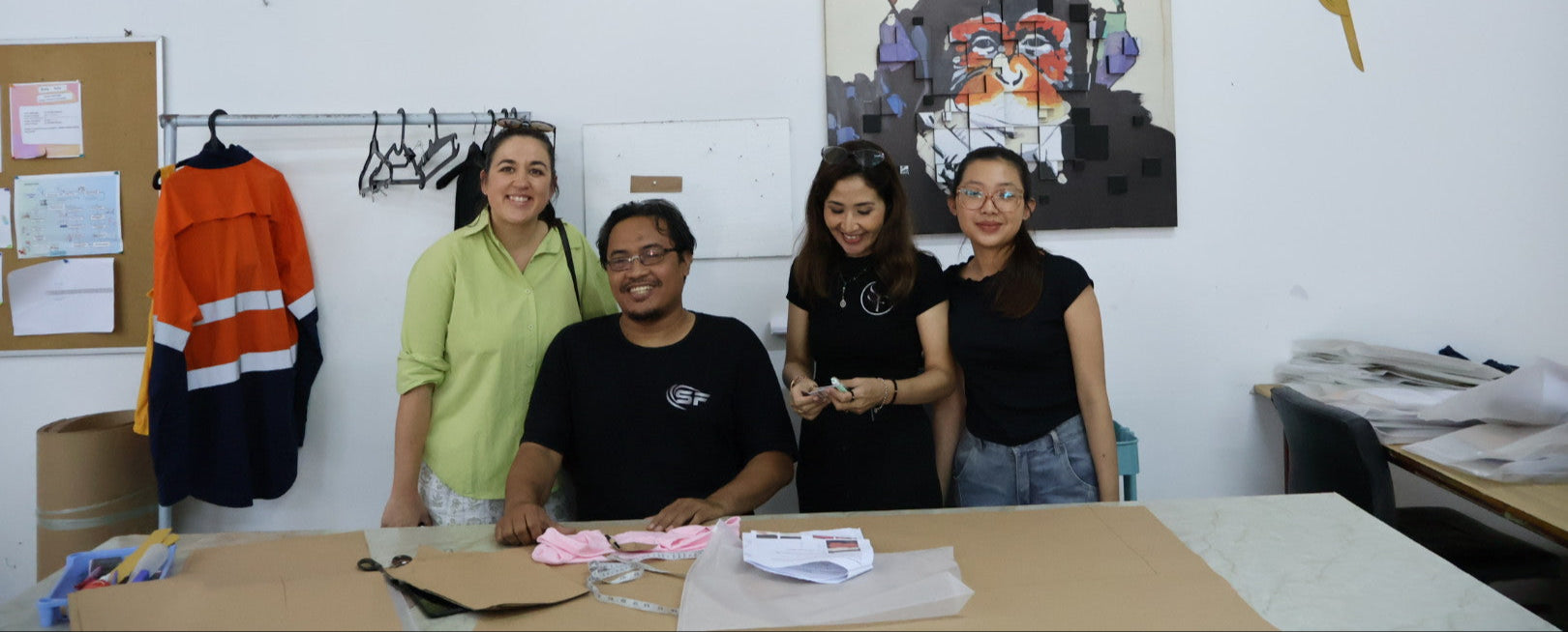 Four people posing together in a workshop or office setting with artwork on the wall.