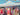 Woman standing in front of a clothing stall with colorful dresses and bunting at an outdoor market.