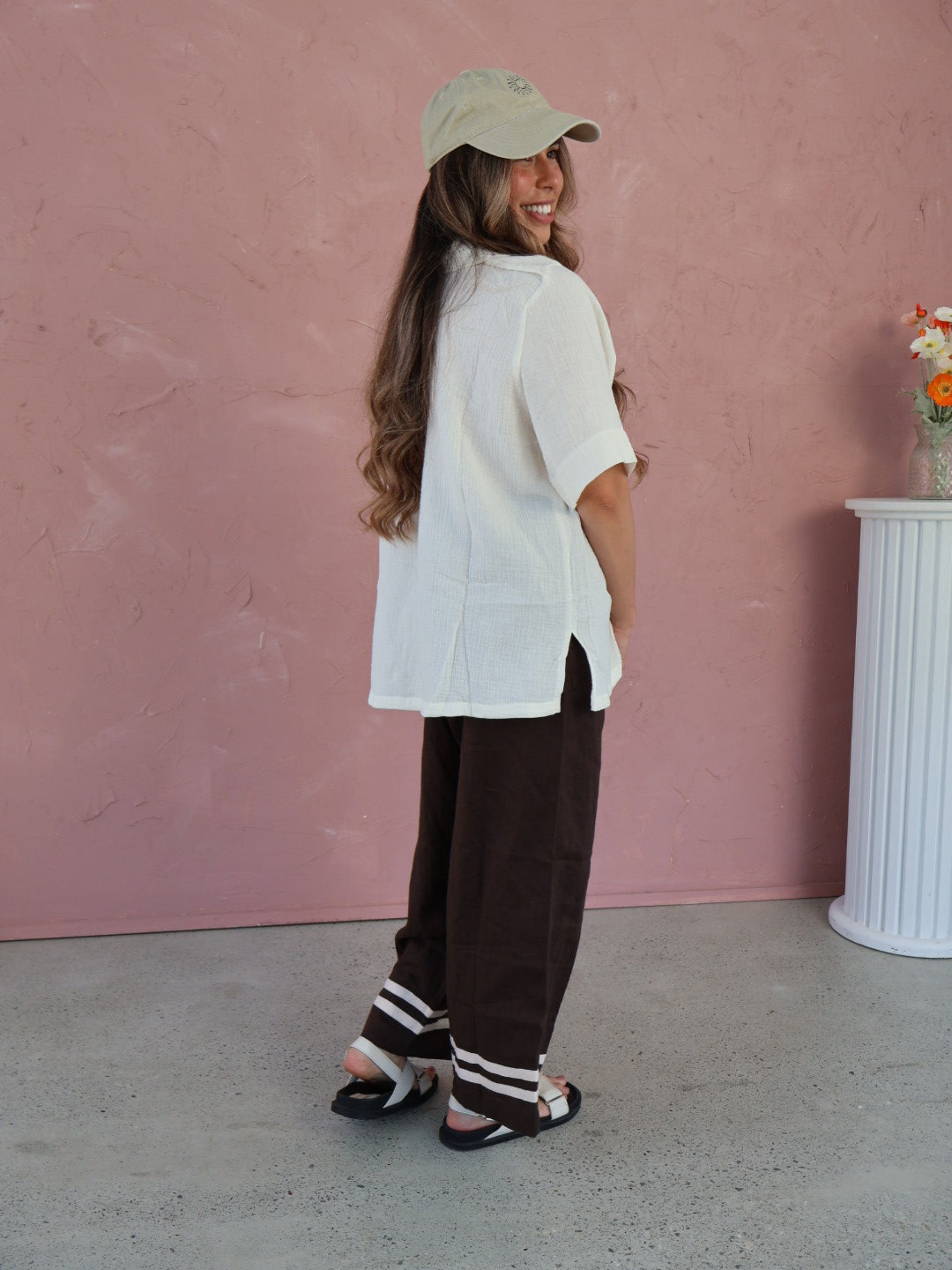 Person wearing a white outfit with a beige cap on a pink floor.
